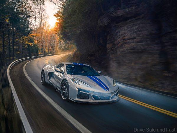 Passenger side front 3/4 view of 2024 Chevrolet Corvette E-Ray 3LZ convertible in Silver Flare with Electric Blue stripe package driving on a curved mountain road. Pre-production model shown. Actual production model may vary. Model year 2024 Corvette E-Ray available 2023.